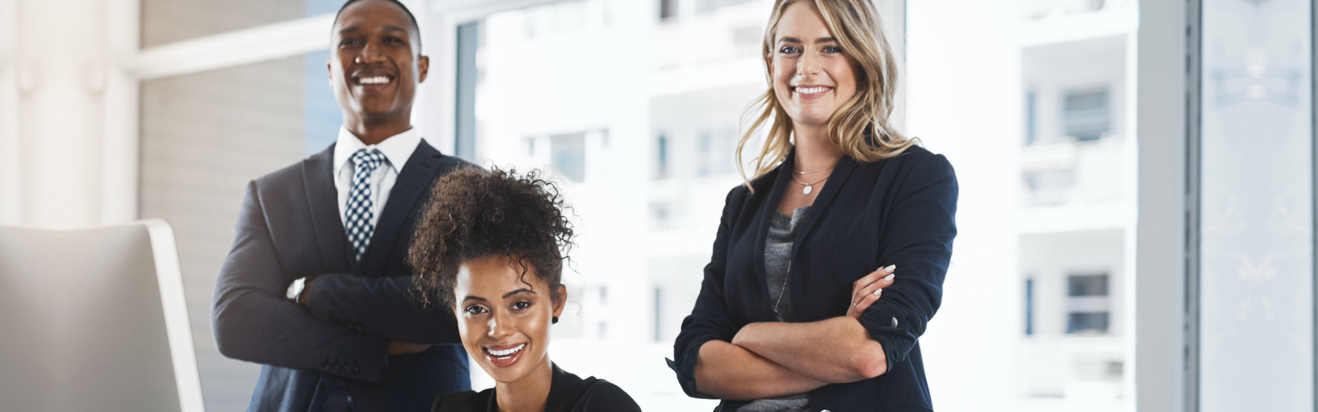 Three professionally dressed individuals standing confidently in an office setting